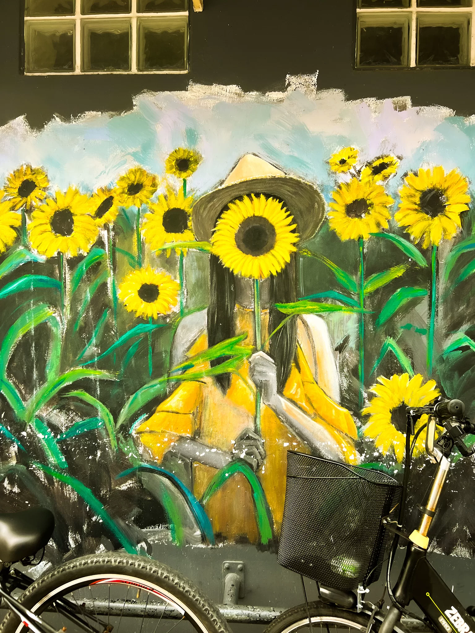 Street art of a female with long hair wearing yellow in a field of yellow sunflowers